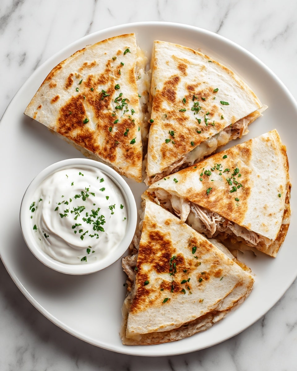 A white plate holds a quesadilla cut into four triangular pieces with a golden brown, slightly crispy outer layer sprinkled with small bits of green herbs. Inside the quesadilla, layers of melted white cheese and light brown shredded chicken are visible. On the side of the plate, a small white bowl filled with smooth white sour cream topped with chopped green herbs sits on a white marbled surface. photo taken with an iphone --ar 4:5 --v 7