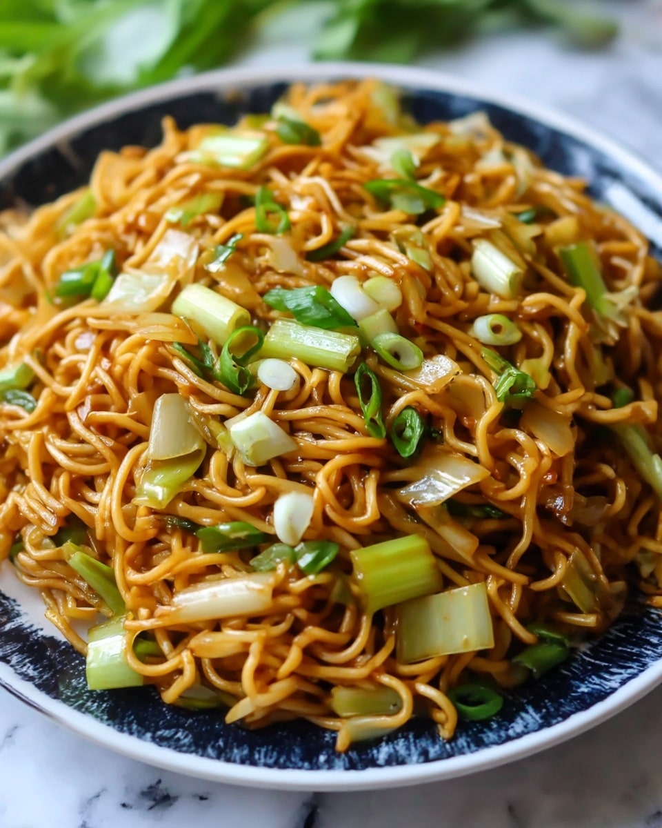 A close-up view of stir-fried noodles on a white plate with a dark blue edge and pattern, showing one main layer of golden-brown noodles mixed evenly with scattered pieces of light green celery, white onion slices, and chopped green onions. The noodles have a slightly glossy texture from sauce, and vegetable pieces are mixed throughout, giving a fresh and colorful contrast. The plate sits on a white marbled surface with some green blurred leaves in the background. photo taken with an iphone --ar 4:5 --v 7