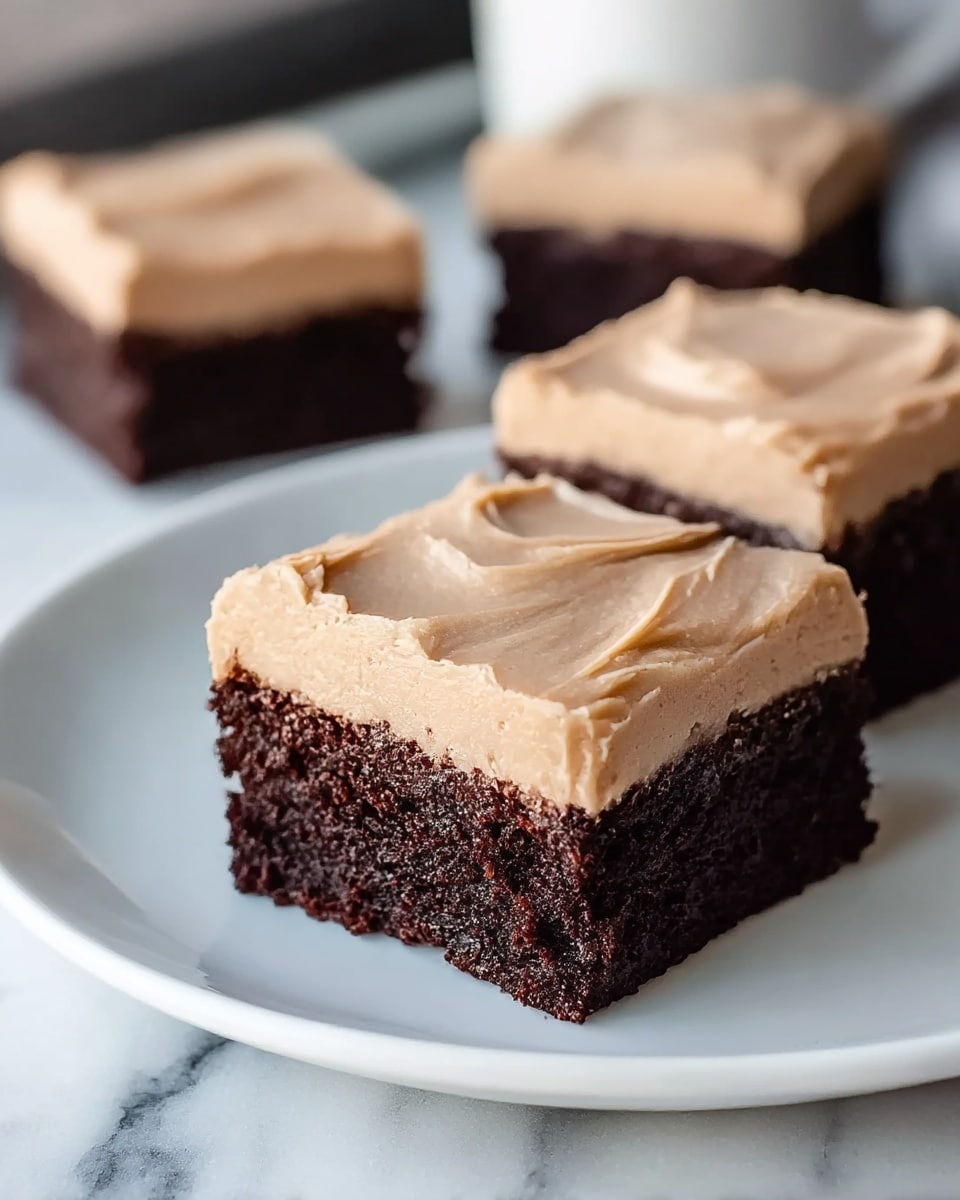 Three square pieces of chocolate cake are shown on a white plate placed on a white marbled surface. Each piece has a thick bottom layer of moist, dark brown chocolate cake with a rough texture and a thick top layer of smooth, creamy light brown frosting. The frosting is evenly spread but has soft swirls and edges. The focus is on the front piece, with two more pieces slightly blurred in the background. Photo taken with an iphone --ar 4:5 --v 7
