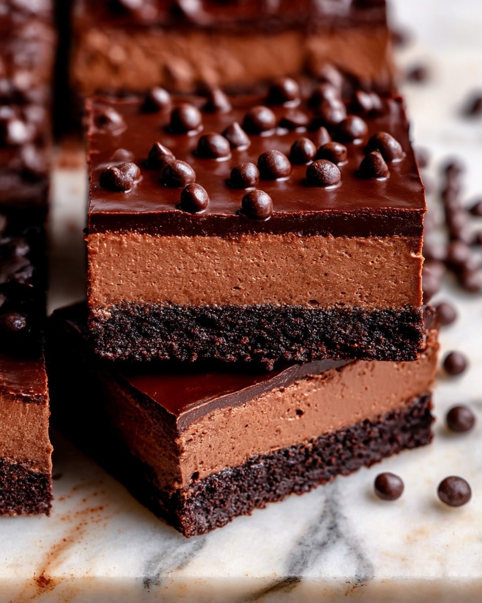 A close-up of rich chocolate bars showing three distinct layers: the bottom layer is dark and dense with a crumbly texture, the middle layer is a lighter, smooth milk chocolate mousse with a creamy appearance, and the top layer is a thick, glossy dark chocolate ganache with small, round chocolate pearls scattered on top. The bars are placed on a white marbled surface with some chocolate pearls scattered around. One bar is positioned slightly tilted on top of the others to show the layers clearly. photo taken with an iphone --ar 4:5 --v 7