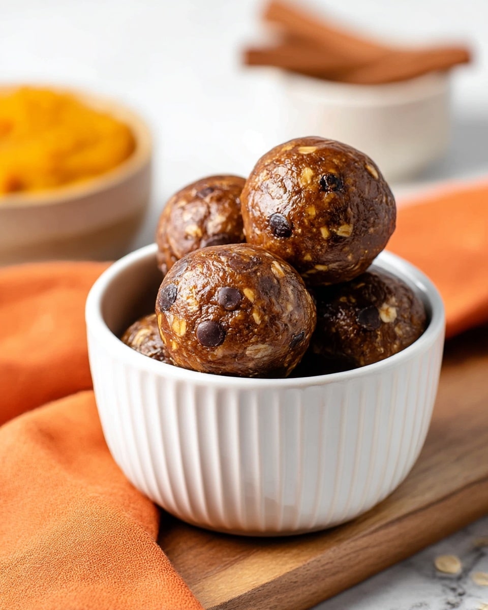 A white, ribbed bowl filled with five round, glossy brown energy balls that have visible oats and dark chocolate chips mixed throughout. The energy balls have a slightly textured and moist surface. The bowl sits on a wooden board next to an orange cloth with a white marbled texture beneath. In the background, two cinnamon sticks and a bowl of orange pumpkin puree are slightly out of focus. photo taken with an iphone --ar 4:5 --v 7