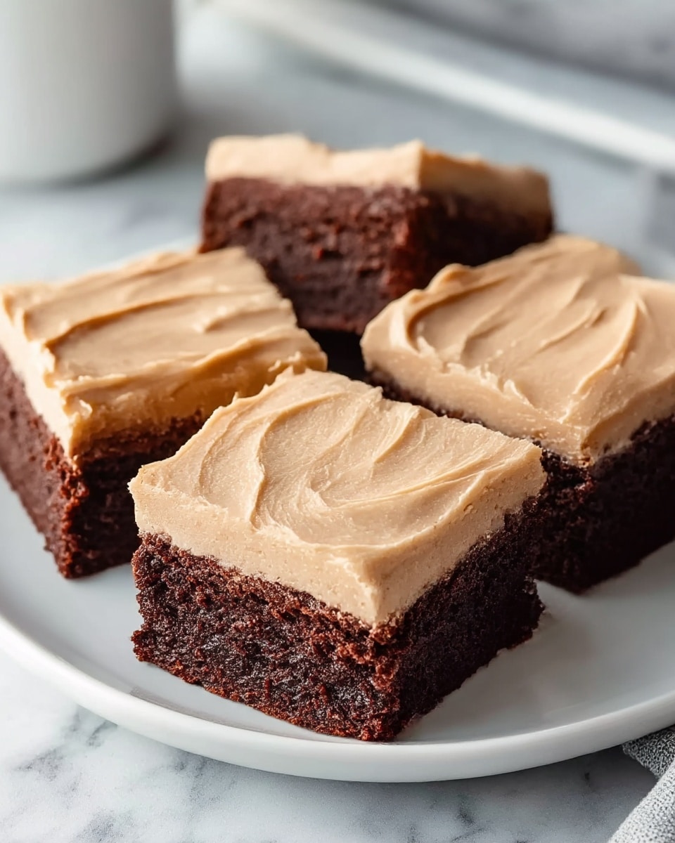 Three square pieces of chocolate cake with a thick layer of smooth light brown frosting on top are placed close together on a white plate. The bottom layer is rich dark brown with a soft, moist texture, while the top layer is creamy and slightly swirled, showing the spread marks of frosting. The background is a white marbled texture, giving a clean and simple look. The photo taken with an iphone --ar 4:5 --v 7