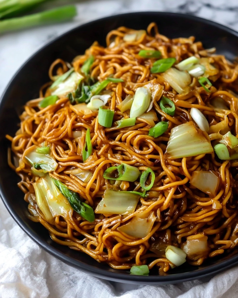 A close-up view of a black bowl filled with a generous layer of cooked noodles coated in a shiny brown sauce mixed with pieces of light green bok choy, white onion chunks, and sliced green onions, spread evenly throughout. The noodles form the main layer, tangled and glossy, with the vegetables adding pops of green and white scattered on top and within. The bowl sits on a white marbled textured surface with part of a white cloth visible near it. photo taken with an iphone --ar 4:5 --v 7
