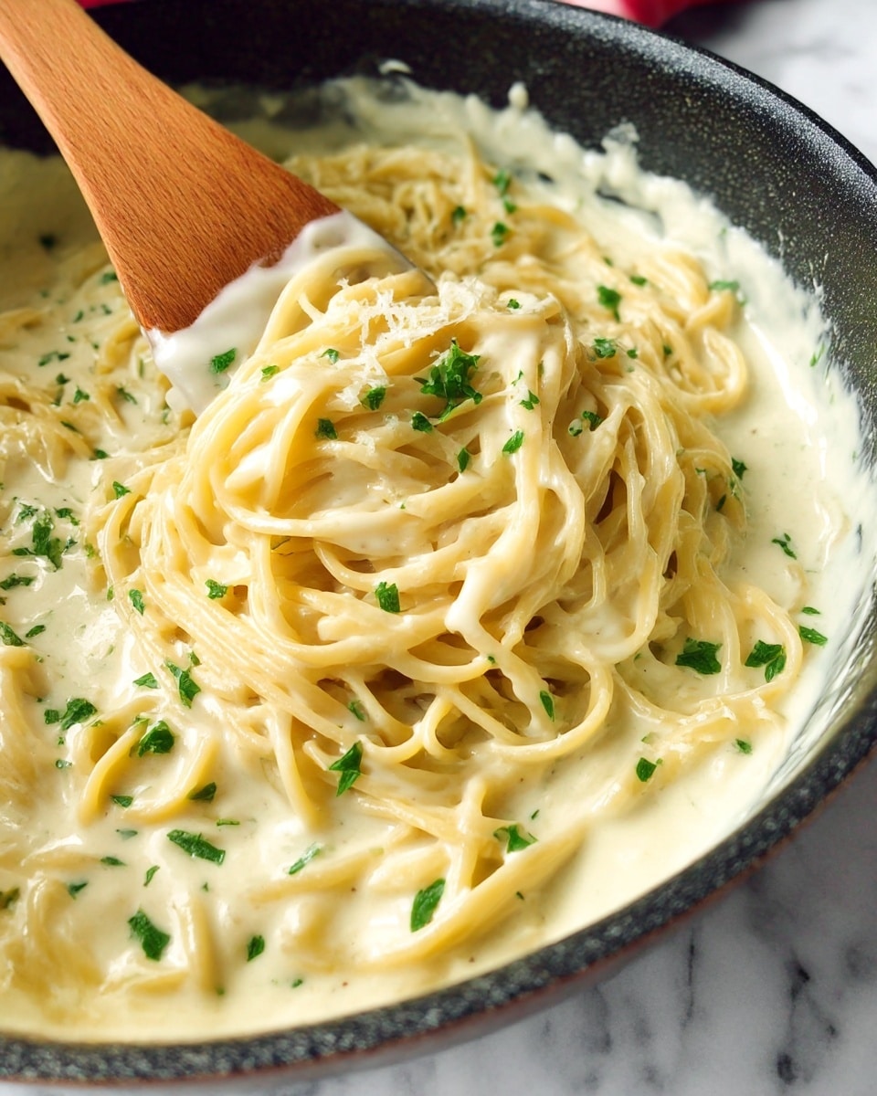 A close-up of creamy spaghetti pasta in a cooking pan, coated in smooth white cheese sauce with small green parsley leaves sprinkled evenly on top, showing thick strands tangled together and a wooden spatula stirring the sauce and noodles, the pan has a dark textured edge and sits on a white marbled surface. photo taken with an iphone --ar 4:5 --v 7