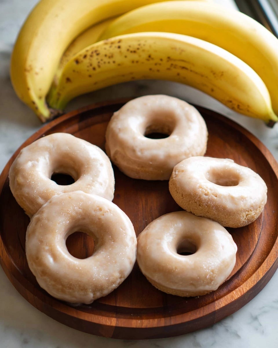 The image shows five light brown donuts with a smooth glaze, each donut round with a hole in the middle, arranged closely on a round wooden board. Behind the board, there are three yellow bananas with small brown spots, resting on a white marbled surface with soft light highlighting the textures. The donuts have a slightly powdery look under the glaze, and the wooden board gives a warm contrast to the light colors of the donuts and bananas. Photo taken with an iphone --ar 4:5 --v 7