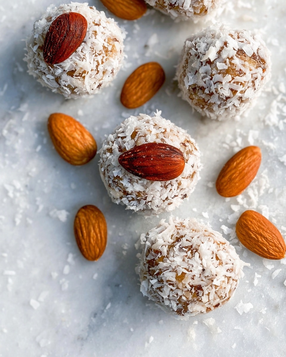 The image shows small round balls with a rough texture covered in white coconut flakes. Each ball is topped with a single whole almond in a brown shade. Around the balls are loose almonds in a light brown color. The background has a white marbled texture with soft gray veins. The balls have a warm brown color peeking through the coconut flakes, giving a contrast of light and dark. The arrangement is casual, with some balls closer and others farther in the frame. Photo taken with an iphone --ar 4:5 --v 7
