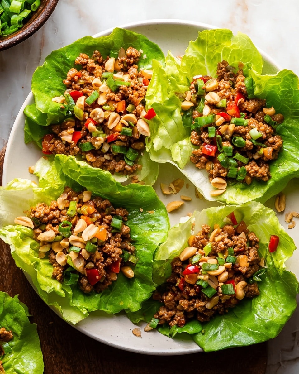 A white plate holds four lettuce wraps, each made from a large, bright green lettuce leaf shaped like a cup. Inside each leaf is a mix of cooked ground meat with small pieces of red and yellow bell peppers, creating a slightly chunky and colorful texture. The top of each wrap is sprinkled with chopped green onions and roughly chopped light tan peanuts, adding contrast and a crunchy texture. The plate sits on a white marbled surface, with a warm light highlighting the freshness and vibrant colors of the dish. photo taken with an iphone --ar 4:5 --v 7