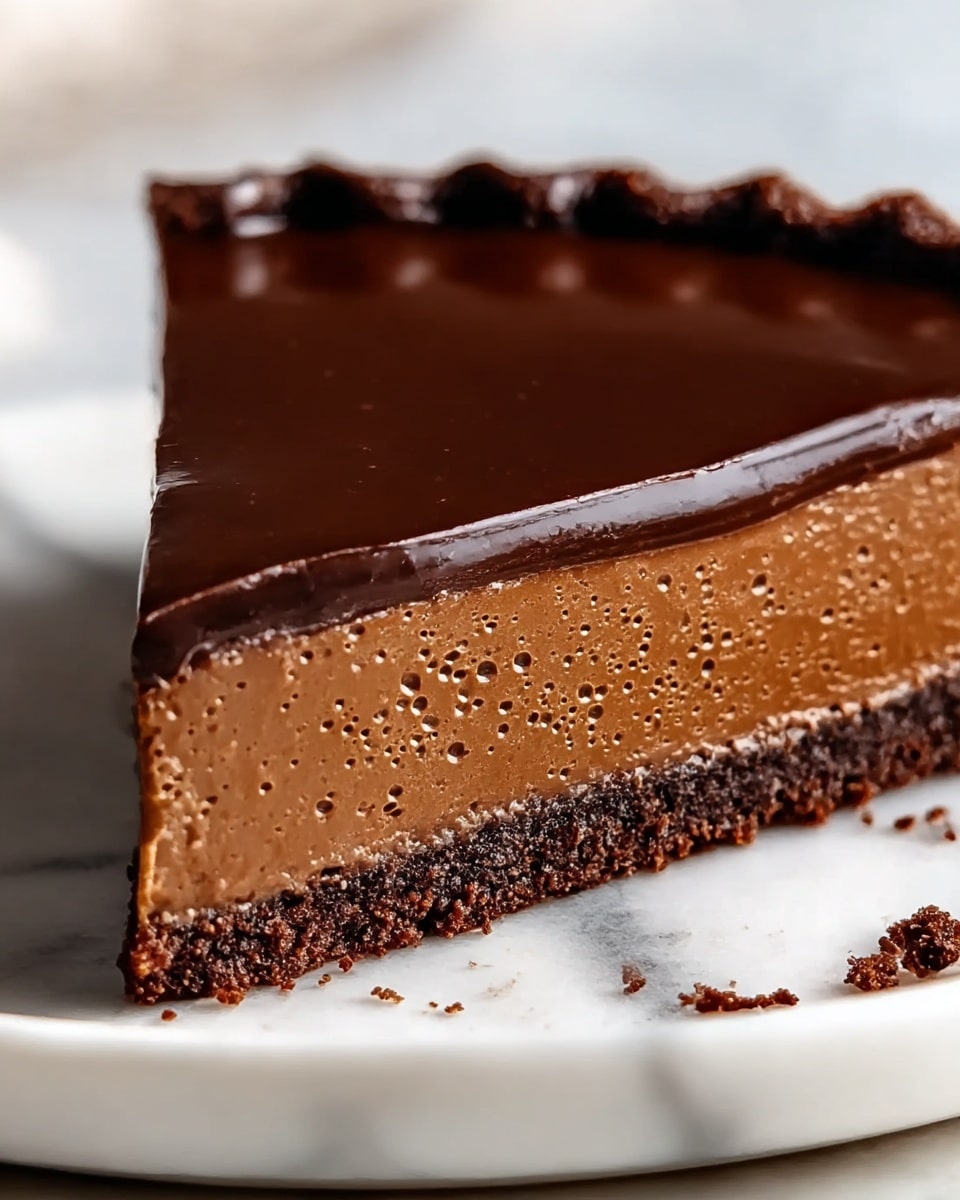 The image shows a close-up of a chocolate tart with three distinct layers, placed on a white plate with a white marbled texture underneath. The bottom crust layer is dark brown and crumbly, appearing thick and slightly rough in texture. Above this is a thick, smooth middle layer of milk chocolate filling that looks creamy and firm with tiny bubbles on the surface. The top layer is a glossy, dark chocolate glaze that is shiny and smooth, slightly dripping over the scalloped edges of the tart crust. Some crumbs are scattered around the base of the tart on the plate. photo taken with an iphone --ar 4:5 --v 7