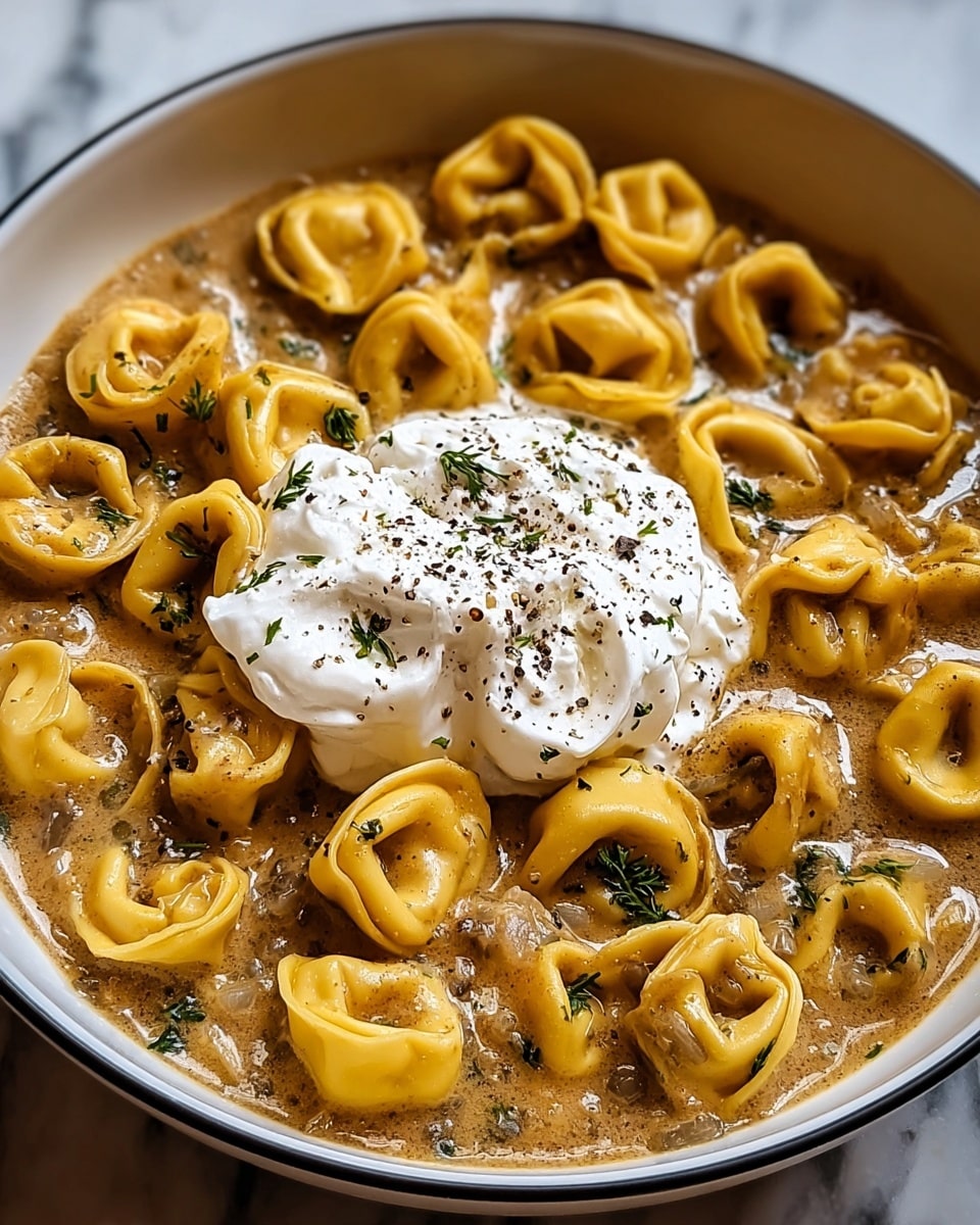 A white bowl filled with three layers: the bottom layer is creamy brown sauce with visible small bits of onion and herbs, the middle layer consists of golden yellow tortellini pasta arranged in a ring around the edge and scattered in the center, and the top layer is a dollop of white, creamy sour cream sprinkled lightly with black pepper sitting in the middle of the bowl, all placed on a white marbled surface. photo taken with an iphone --ar 4:5 --v 7