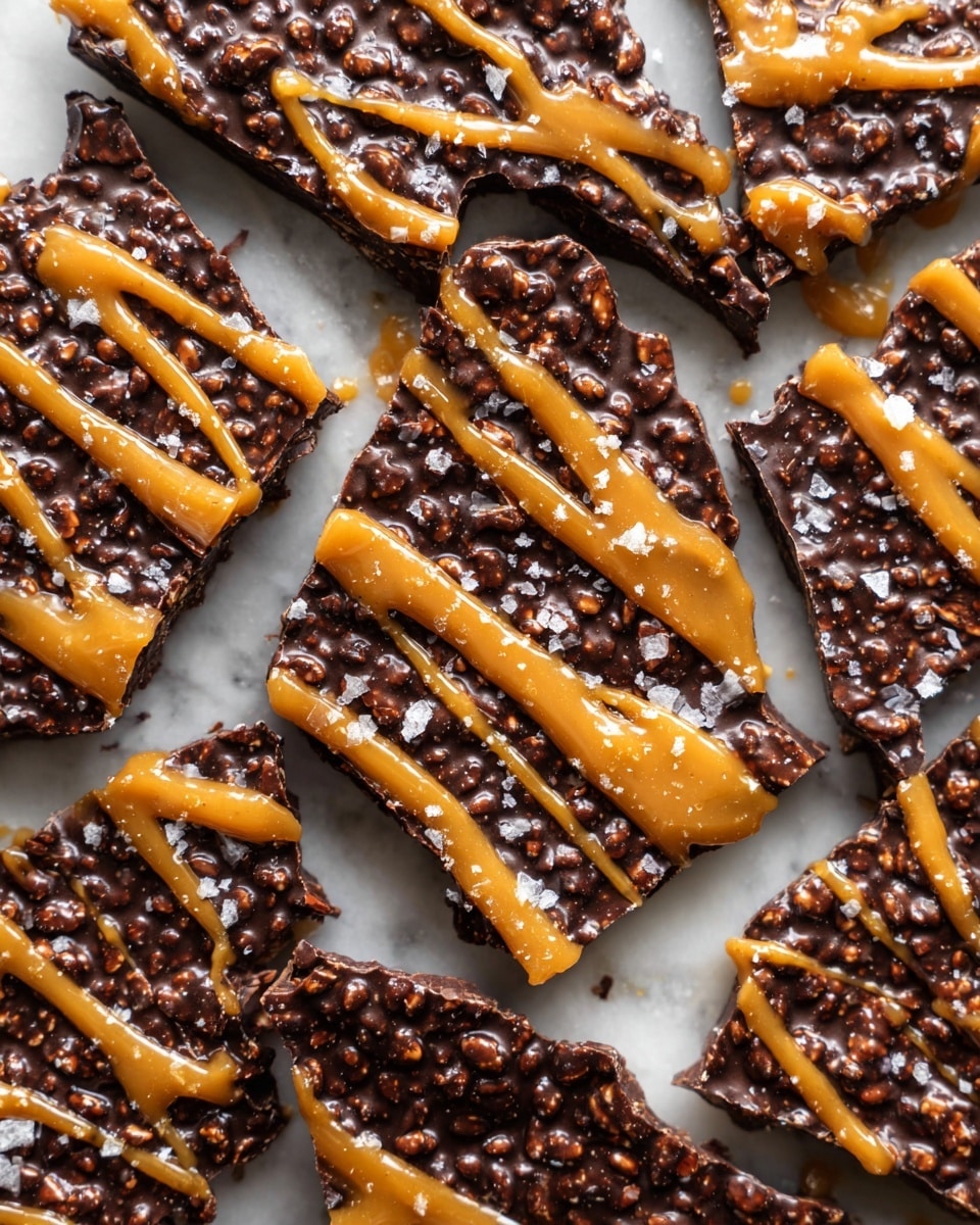 The image shows several pieces of chocolate crispy bark broken into irregular shapes, arranged closely on a white marbled surface. Each piece has two distinct layers: a textured dark chocolate base embedded with crispy puffed grains giving a bumpy surface, and a golden caramel-colored drizzle spread unevenly over the top in thick, shiny lines. Tiny flakes of sea salt are scattered on the chocolate and caramel, adding bright white specks that contrast with the deep brown and amber colors. The overall look is rich and crunchy with glossy highlights on the caramel streaks. photo taken with an iphone --ar 4:5 --v 7