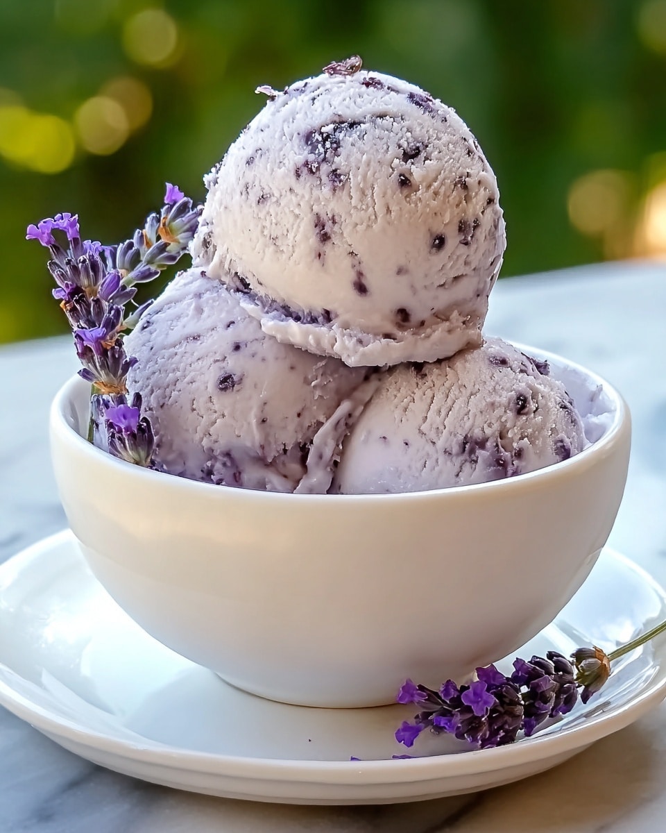 A white bowl holds three scoops of lavender ice cream with small dark specks inside, stacked neatly on top of each other, showing a smooth but slightly textured surface with frozen edges. The ice cream is pale purple, and a few fresh purple lavender flowers decorate the side of the bowl and top scoop. The bowl sits on a white plate on a white marbled surface, with a blurred green background that suggests an outdoor setting. photo taken with an iphone --ar 4:5 --v 7