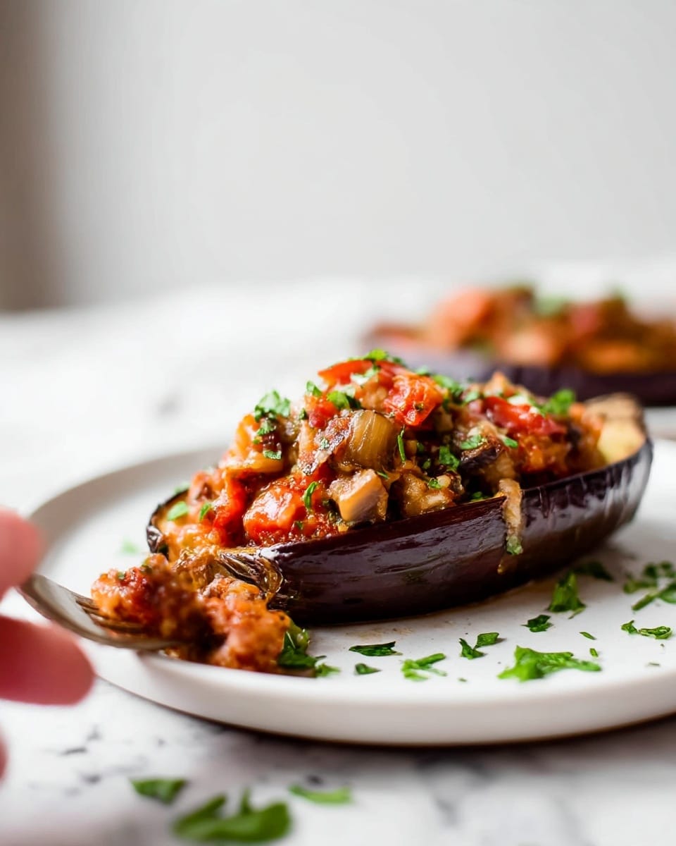 Four stuffed eggplant halves are neatly placed in a white ceramic baking dish with a glossy finish. Each eggplant half has a dark purple outer skin and soft light brown inner flesh, filled with a mixture of browned ground meat, diced red tomatoes, and melted white cheese, creating a textured and slightly golden top. Small bits of fresh green herbs are sprinkled over the filling and around the dish, adding a fresh pop of color. The dish rests on a white marbled surface, and a beige textured cloth with a brass spoon is partially visible in the background. photo taken with an iphone --ar 4:5 --v 7