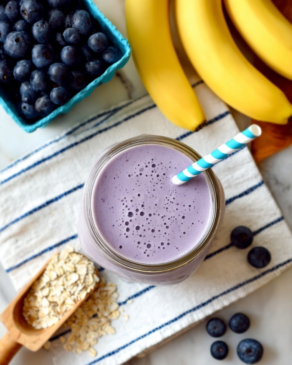 A top view of a glass jar filled with a smooth, light purple smoothie, showing small bubbles on the surface, with a blue and white striped straw inserted inside. The jar is placed on a white cloth with thin blue stripes on a white marbled surface. To the upper left side, there is a blue carton box filled with fresh dark blue blueberries. Next to it, a wooden scoop with light beige oats spilling on the surface. In the upper right corner, three yellow bananas lay side by side. A few scattered blueberries are also visible on the white marbled surface near the jar. Photo taken with an iphone --ar 4:5 --v 7