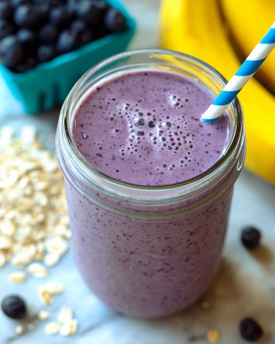 A close-up view of a purple smoothie inside a clear glass jar filled to the top, textured with tiny dark specks and bubbles on the surface. A blue and white striped straw is placed on the right side, going into the smoothie. Around the jar, there are blurred ingredients including a white marbled surface, a light blue container of dark blueberries on the left, some rolled oats scattered on the left, and a group of yellow bananas in the background. The smoothie is the main focus of the image. Photo taken with an iphone --ar 4:5 --v 7