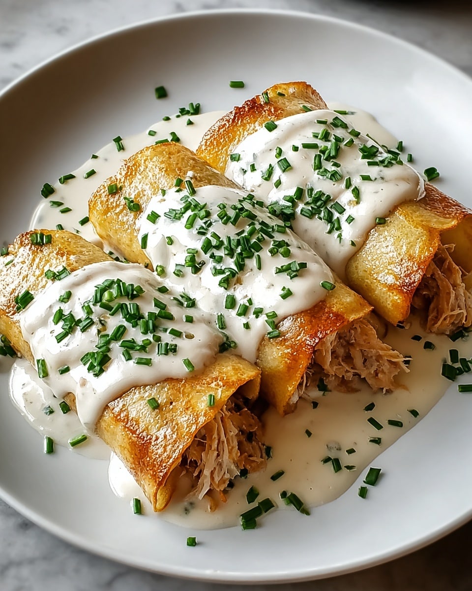 Two golden brown rolled crepes filled with a creamy shredded chicken mixture sit side by side on a white plate. Each crepe is topped with a thick layer of white sauce, sprinkled generously with green chopped chives and a light layer of golden crispy crumbs. The creamy sauce also pools around the base of the crepes, blending with the chicken filling that peeks out slightly. The plate is set against a white marbled surface. photo taken with an iphone --ar 4:5 --v 7