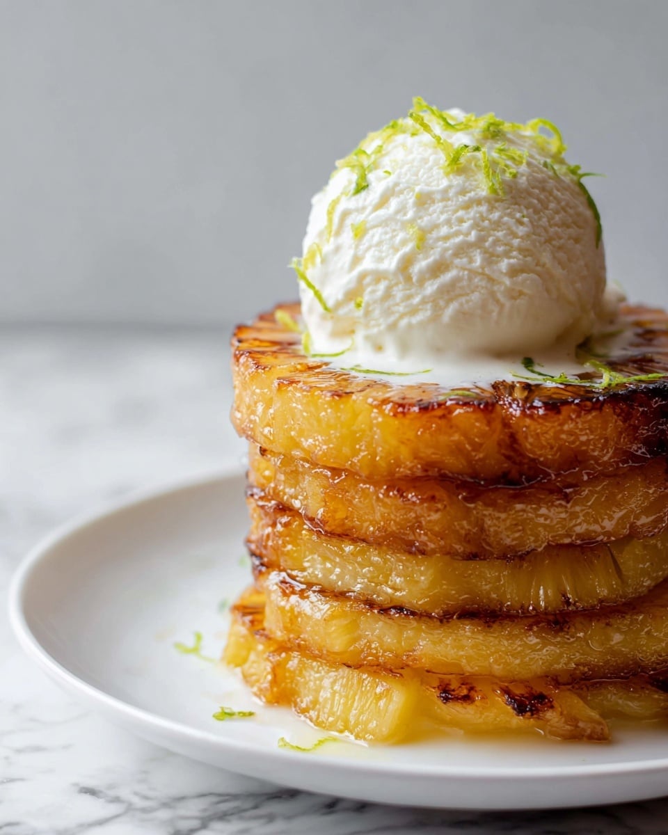 A tower of four golden-brown grilled pineapple slices sits in the center of a white plate, each slice showing a caramelized texture with slightly crispy edges and juicy interior. On top of the pineapple stack, there is one large scoop of creamy off-white ice cream with a smooth texture, melting slightly and creating soft drips over the pineapple layers. The ice cream is garnished with tiny green lime zest shreds, adding a fresh color contrast. The background features a white marbled texture, giving a clean and bright look to the image. photo taken with an iphone --ar 4:5 --v 7