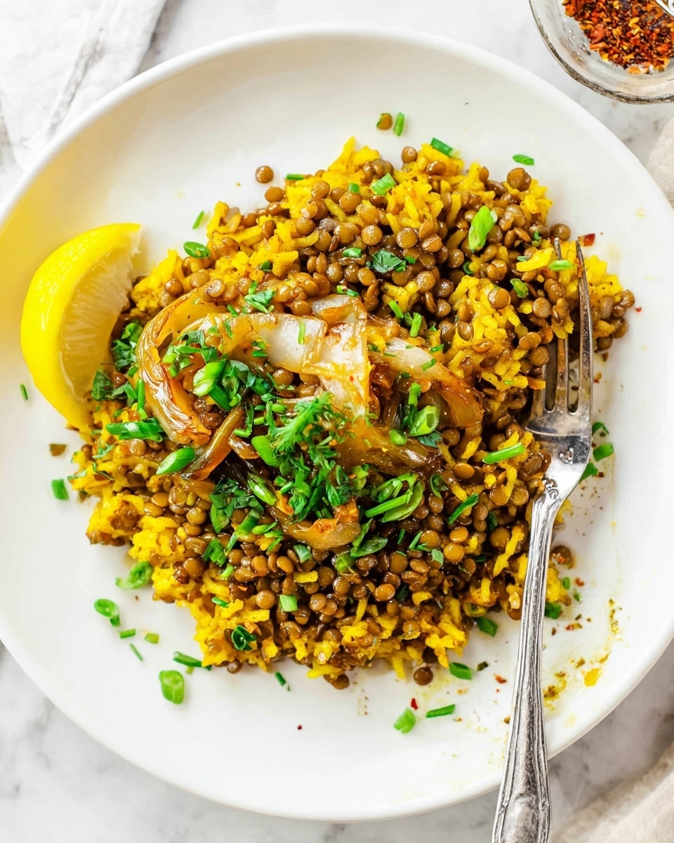 A white plate on a white marbled texture holds a serving of yellow rice mixed with green lentils, creating a chunky, textured layer that fills most of the plate. There are caramelized onions with a glossy, brownish-orange tint scattered across the dish. Bright green chopped scallions are sprinkled on top, adding a fresh contrast. A lemon wedge rests near the edge of the rice. A silver fork lies on the plate's right side, partly on the food. Small drops of oil and spice flakes are scattered lightly around the plate’s edge, giving a casual, inviting look. Photo taken with an iphone --ar 4:5 --v 7