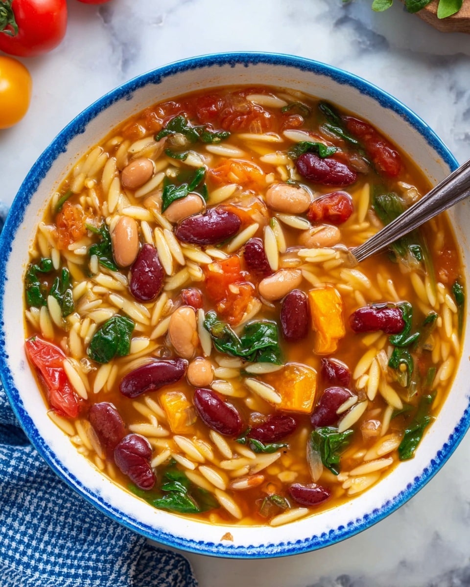 A bowl of soup with three main layers is shown. The bottom layer is a golden-orange broth, warm and clear. The middle layer has small off-white orzo pasta, along with bright red kidney beans and light brown beans scattered throughout. The top layer shows chunks of cherry tomatoes, some orange slices of squash or carrot, and pieces of dark green leafy spinach. A silver spoon is partially submerged on the right side of the bowl. The bowl itself is white with a blue rim, set on a white marbled surface, with some tomatoes and a blue checked cloth partially visible around it. Photo taken with an iphone --ar 4:5 --v 7