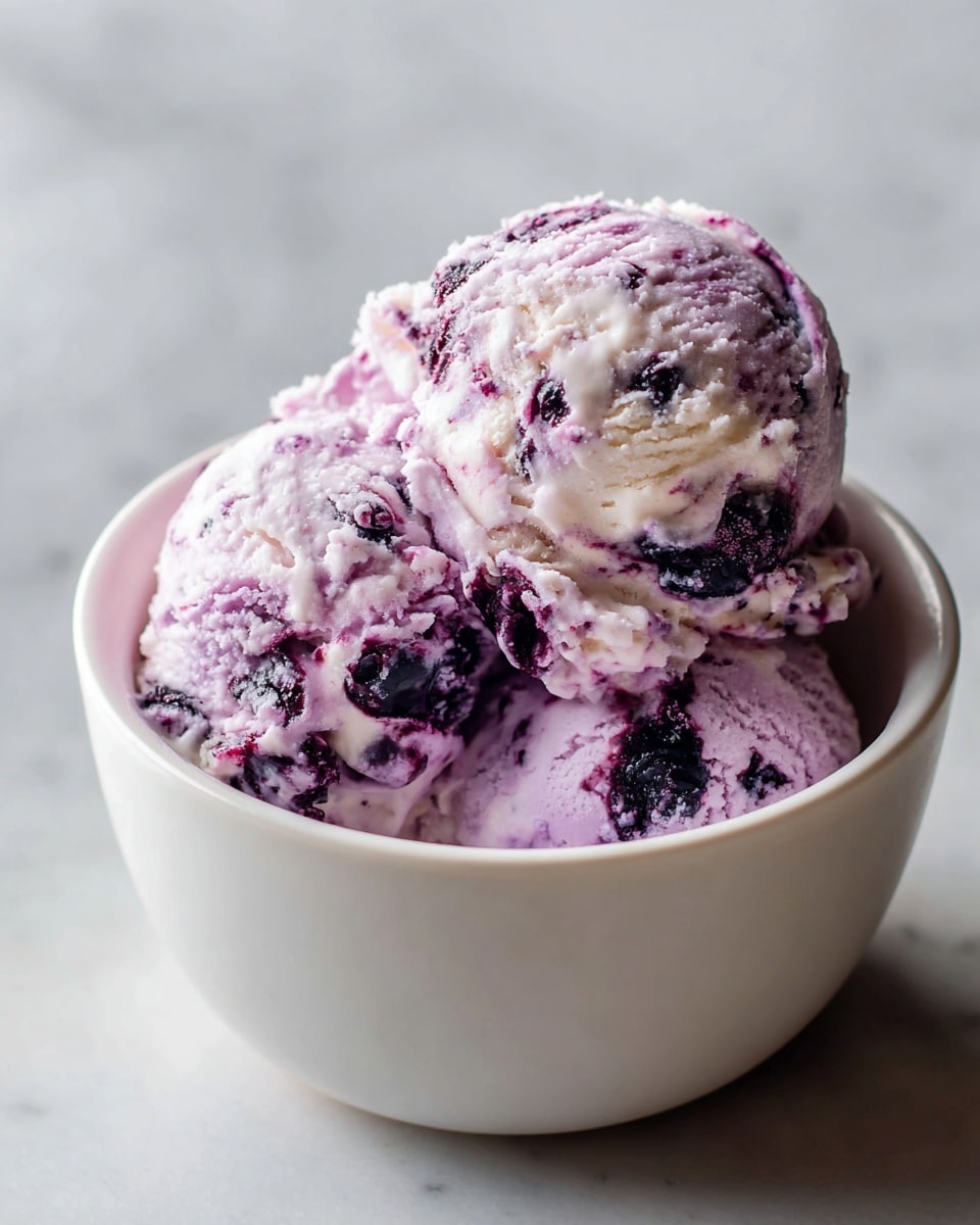 A white bowl filled with two large scoops of creamy purple and white ice cream with dark purple fruit chunks swirled throughout. The texture of the ice cream looks smooth and slightly soft with visible berry pieces embedded in the layers. The bowl sits on a surface with a white marbled texture in soft natural light, enhancing the colors and creamy texture of the ice cream. photo taken with an iphone --ar 4:5 --v 7